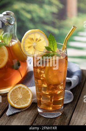 Bicchiere di tè freddo con fette di limone e menta un tavolo di legno con sfondo rurale Foto Stock