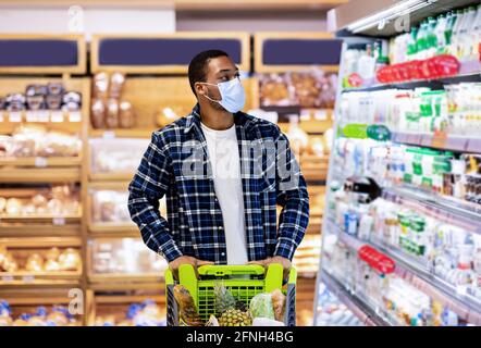 Giovane ragazzo nero in maschera monouso selezionando prodotti caseari al deposito durante la quarantena di covid Foto Stock