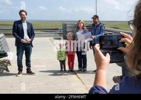 Nordstrandischmoor, Germania. 17 maggio 2021. Ruth Kruse (r) Fotografie Jan Philipp Albrecht (l, Bündnis 90/Die Grünen), Ministro dell'ambiente di Schleswig-Holstein, Stefanie (3° da destra) e nomme (2° da destra) con i figli Bosse ed Emma. Albrecht ha presentato alla famiglia sul Hallig Nordstrandischmoor una sovvenzione per il Norderwarft. Attualmente è in fase di sviluppo nel primo tumulo di abitazioni controllate dal clima del mondo. Credit: Frank Molter/dpa/Alamy Live News Foto Stock