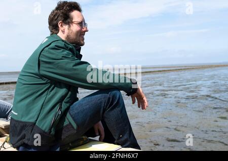 Nordstrandischmoor, Germania. 17 maggio 2021. Jan Philipp Albrecht (Bündnis 90/Die Grünen), ministro dell'ambiente dello Schleswig-Holstein, si trova su un carrello e si affaccia sul Mare del Nord. Sull'Hallig Nordstrandischmoor, Albrecht ha consegnato una notifica di finanziamento per il Norderwarft. Attualmente è in fase di espansione per diventare il primo tumulo di abitazioni a controllo climatico al mondo. Credit: Frank Molter/dpa/Alamy Live News Foto Stock