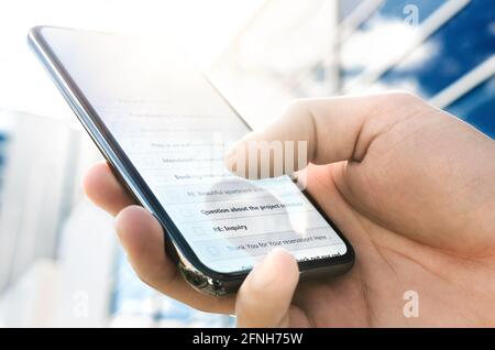 Posta in arrivo con elenco messaggi nel telefono. Uomo d'affari che utilizza uno smartphone fuori dal moderno ufficio aziendale della città in una mattina soleggiata. Foto Stock