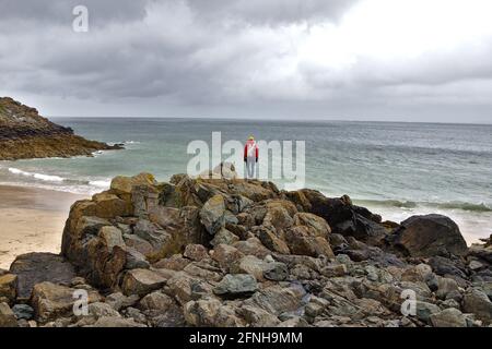 Donna in piedi in cima ad uno sperone roccioso che domina la spiaggia di Porthgwidden Cornovaglia Foto Stock