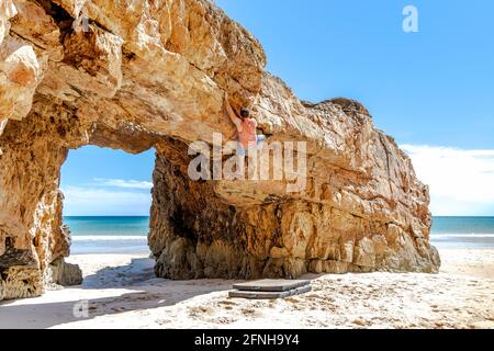 Giovane scalatore di roccia salendo in modo sicuro una scogliera gialla ad Algarve, Portogallo Foto Stock