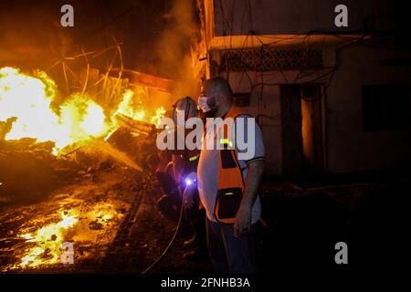 15 maggio 2021: Gaza, Palestina. 15 maggio 2021. Gli equipaggi della Difesa civile palestinese lavorano per spegnere un incendio che ingolce una fabbrica agrochimica a seguito di un bombardamento israeliano a Beit Lahia, nella striscia di Gaza settentrionale. Il bombardamento di Gaza con le incursioni aeree israeliane e il fuoco di artiglieria è proseguito venerdì per il quarto giorno consecutivo, mentre le fazioni palestinesi hanno sparato un'altra serie di razzi verso Israele. La violenza in atto tra le due parti ha continuato a intensificarsi con più di 120 palestinesi uccisi a Gaza e 950 feriti. 9 israeliani sono stati uccisi e più di 13 Foto Stock