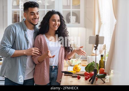 Giovane coppia araba che usa lo smartphone sul treppiede in cucina per Registrazione Vlog Foto Stock