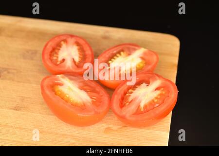 Quattro metà di un pomodoro rosso su un tagliere di legno, primo piano, su sfondo nero. Foto Stock