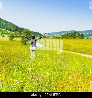 Donna con braccia aperte. In estate nel campo. Fiori di prato e erba alta. Foto Stock