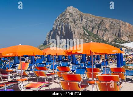 San Vito lo Capo, Trapani, Sicilia, Italia. Splendidi mobili da spiaggia sulla spiaggia affollata, l'imponente parete nord del Monte Monaco sullo sfondo. Foto Stock