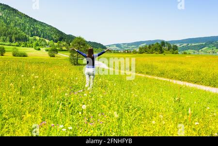 Donna con braccia aperte. In estate nel campo. Fiori di prato e erba alta. Foto Stock