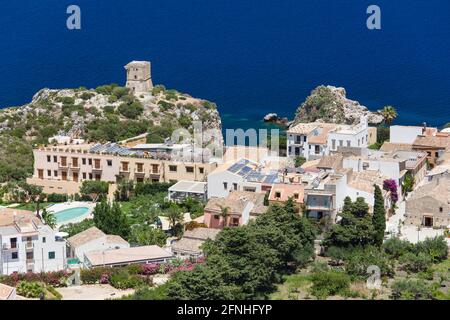 Scopello, Trapani, Sicilia, Italia. Vista sui tetti del villaggio fino all'antica torre di guardia sulle scogliere sopra le acque blu del Golfo di Castellammare. Foto Stock