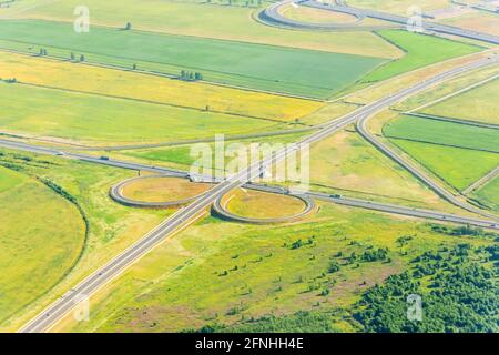 Scambio cloverleaf visto dall'alto. Vista aerea del bivio autostradale in campagna con alberi e campi coltivati. Occhio di uccello. Foto Stock