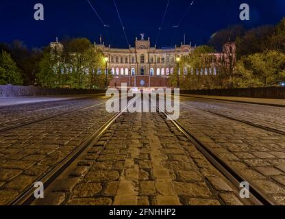 Vista simmetrica in prospettiva bassa su una pista del tram con la famosa architettura di Monaco sullo sfondo di notte. Foto Stock