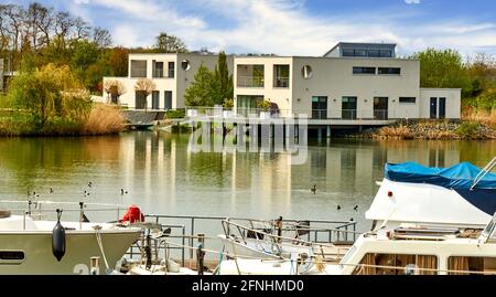 Vista sul porto turistico di Bortfeld, Germania, con le navi in primo piano e lussuose ville moderne sulla riva sullo sfondo Foto Stock