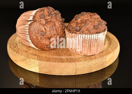 Due deliziosi muffin al cioccolato su un vassoio di legno rotondo, primo piano, su sfondo nero. Foto Stock