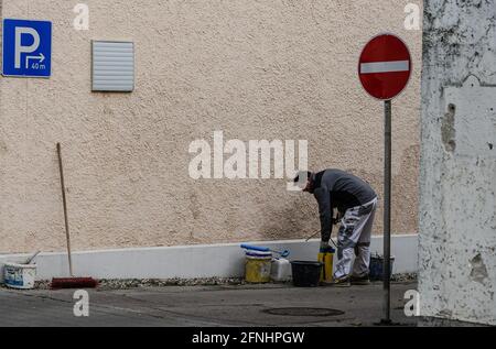 Un pittore si alza piegato sopra con i secchi di vernice e degli attrezzi davanti ad un muro della casa che deve essere verniciato. Foto Stock