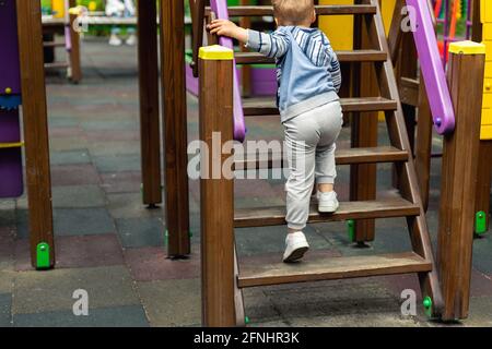 Indietro vista adorabile caucasico biondo piccolo bambino bambino divertitevi a salire le scale di legno nel moderno parco giochi per bambini in estate brillante Foto Stock