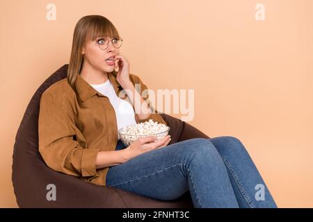 Foto di giovane donna spaventato morso unghie guardare film horror mangiare popcorn isolato su sfondo di colore beige Foto Stock