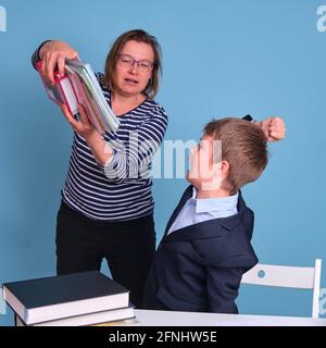 Conflitto tra una madre e un ragazzo di scuola che si rifiuta di imparare, sfondo blu Foto Stock