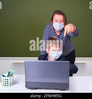 Insegnante e scolaro durante l'apprendimento a distanza nella scuola elementare, concetto di problemi su sfondo lavagna Foto Stock