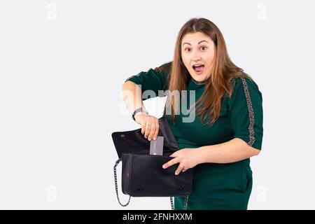 Primo piano di donna caucasica portare elegante borsa nera sulla spalla e tenendo carta di credito, concetto per shopaholic ragazza, isolato su grigio Foto Stock