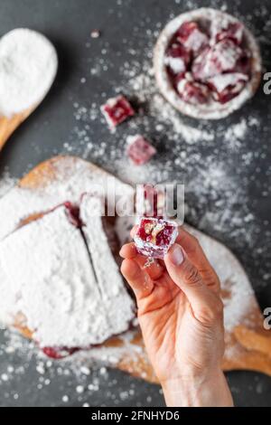 Una donna sta tenendo un pezzo a forma di dadi di frutta e frutta aromatizzata in casa delizia turca ricoperta di zucchero di pasticceria in polvere. In background in Foto Stock