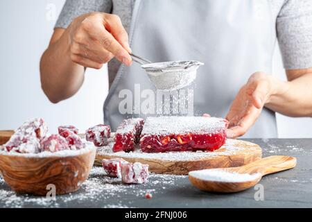 Produzione di deliziosa frutta aromatizzata in casa turca delizia con vivace colore rosa rosso e mescolato con nocciole. Si aggiunge zucchero a velo setacciato Foto Stock