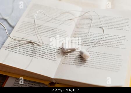 primo piano di auricolari bianchi su libri sfocati Foto Stock