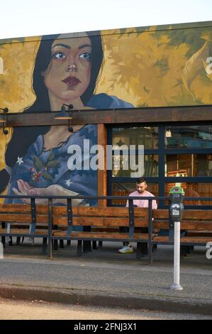Giovane uomo seduto al di fuori di un ristorante sulla Main Street a Mount Pleasant, Vancouver, British Columbia, Canada Foto Stock