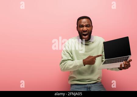eccitato afroamericano che punta al laptop con schermo vuoto su sfondo rosa Foto Stock