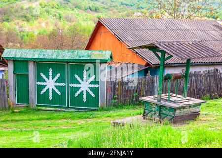 Pozzo d'acqua di fronte alla casa di campagna. Tradizionale casa rustica con cancello in legno Foto Stock