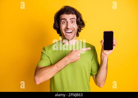 Foto di positivo uomo tenere telefono diretto dito schermo vuoto space wear t-shirt verde isolato di colore giallo sfondo Foto Stock