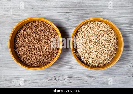 vista dall'alto del grano saraceno torrefatto e verde in ceramica rotonda ciotole su tavola di legno grigio Foto Stock