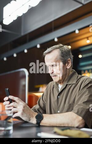 Uomo maturo concentrato con baffi seduti a tavola e utilizzando internet mobile su smartphone nel caffè con wifi gratuito Foto Stock