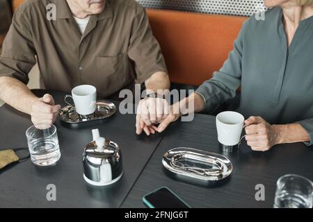Primo piano di una coppia caucasica matura seduta a tavola e tenuta mani mentre si beve il tè insieme nella caffetteria Foto Stock