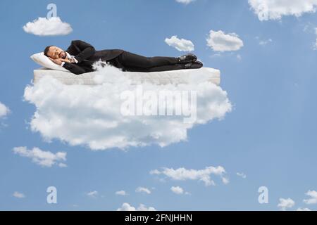 Uomo d'affari in un vestito e cravatta dormendo su un materasso e galleggianti su nuvole e un cielo blu Foto Stock