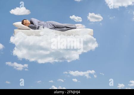 Uomo in pigiama che dorme su un materasso e galleggia nuvole e un cielo blu Foto Stock