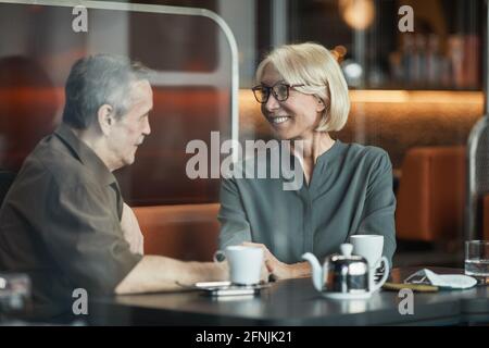 Donna caucasica anziana felice in occhiali seduti a tavola e. tenendo la mano del ragazzo mentre lo guarda con amore in caffetteria Foto Stock