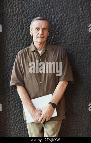 Ritratto del soddisfare bello uomo caucasico anziano in piedi orologio da polso con notebook contro pareti in pietra nera Foto Stock