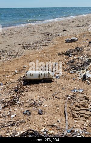 Una vecchia bottiglia di plastica semi-decomposta, sacchetti di plastica e altri rifiuti giacciono sulla riva tra le conchiglie sulla sabbia. Inquinamento ambientale concep Foto Stock