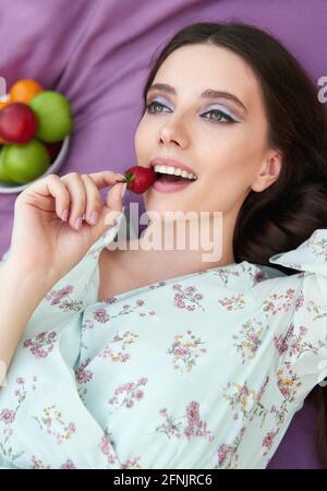 Bella ragazza sorridente mangia fragola. Primo piano ritratto della bella giovane donna in abito Foto Stock