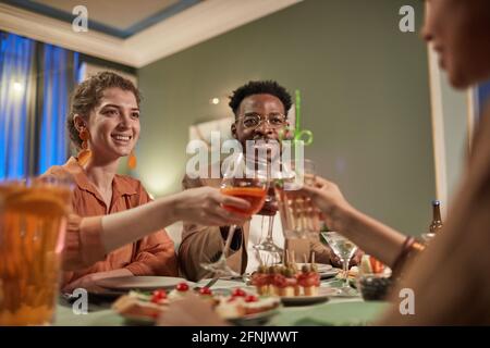 Ritratto ad angolo basso di una coppia di regate miste che si gode la cena con gli amici al chiuso e occhiali da clinking sopra il tavolo festivo, spazio copia Foto Stock