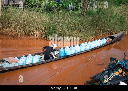 Shan state, Myanmar - 7 gennaio 2020: La barca tradizionale trasporta molte bottiglie di acqua blu attraverso un canale fangoso vicino al lago di Inle, Nyaung Shwe Foto Stock