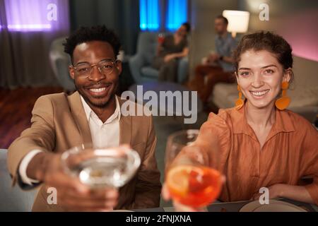 Ritratto di un'elegante coppia mista che si gode la cena con gli amici all'interno e tostatura sulla fotocamera Foto Stock