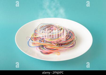 Cavi colorati su una piastra da cui fuoriesce vapore su sfondo blu. Un concetto ispirato agli spaghetti e al cibo. Stile fotografico minimo. Foto Stock
