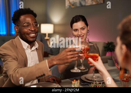 Ritratto di un'elegante coppia mista che si gode la cena con gli amici all'interno e tostando sopra il tavolo festivo Foto Stock