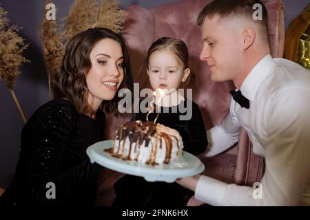 La bambina soffia fuori le candele sulla torta con i suoi genitori Foto Stock