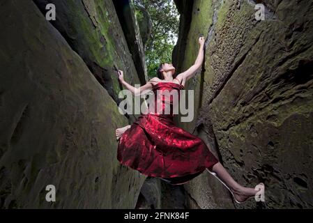 Donna bouldering sulle rocce di arenaria in abito rosso Foto Stock