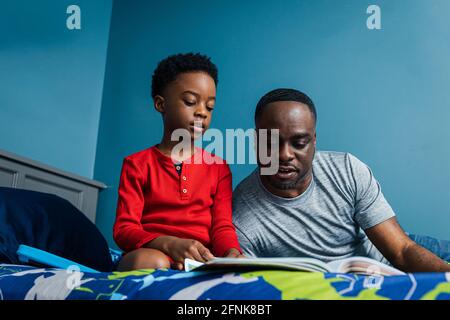 Padre che lavora con il figlio sui suoi compiti a casa il letto Foto Stock
