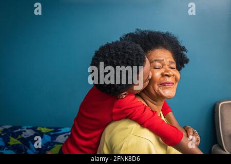 Nipote che bacia la nonna sulla guancia dalla parete blu a casa Foto Stock