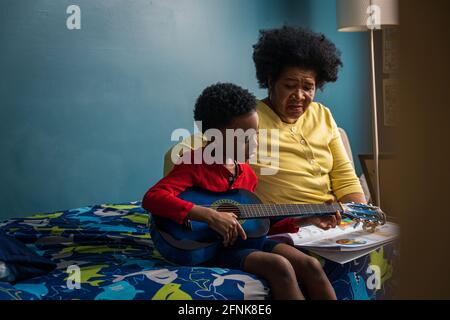 Nonna che guarda il nipote che pratica la chitarra a casa Foto Stock